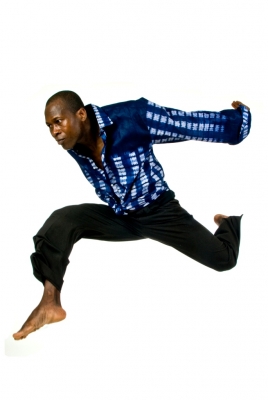 Etienne jumps in a blue shirt with arms stretched behind him 