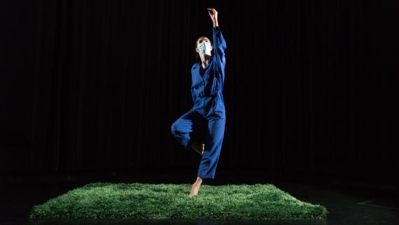 A woman in a blue jumpsuit dances on a patch of grass