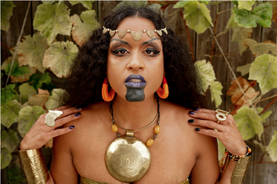 Brown skinned woman adorned in African gold jewelry and black paint. 