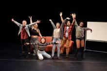 Dancers pose in front of a couch with their arms stretched out 