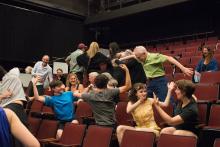 audience members wave their arms and wiggle their bodies as part of graduate symposium lecture. 