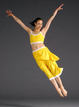 Lady in yellow jumps with arms in wide 'V' shape and legs straight and together. 
