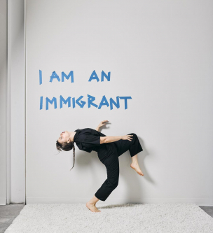 Alice dances front of a wall that says, "I am an immigrant" 