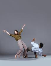 Sarah and Brian fall backwards away from each other. On the left, Sarah has her arms in a wide 'V' shape over her head as she hinges at her knees. On the right, Brian's back is barely off the floor. 