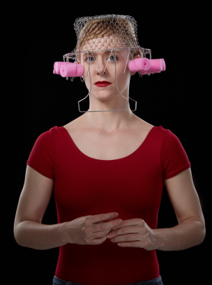 Lady in red shirt and lipstick with wire basket and foam hair curlers on head. 
