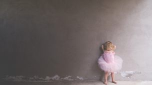 A little girl in ballet clothing standing at a wall 