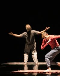 A woman in a twisted, active pose in the foreground and a man with his arms wide and his back to the camera in the background
