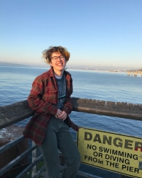 Andy smiles in front of water by a danger sign