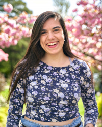Michelle Asencio smiles in front of pink flowers