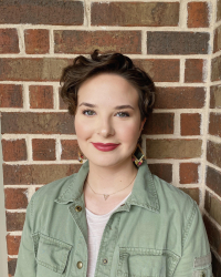 Brooke Thimmig in a green jacket infant of a brick wall