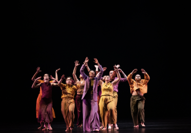 UW Dancers in colorful clothing on stage with their hands up 
