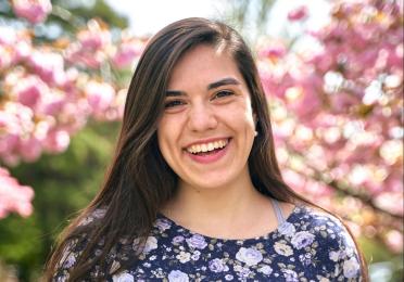 Michelle Asencio smiles in front of pink flowers 
