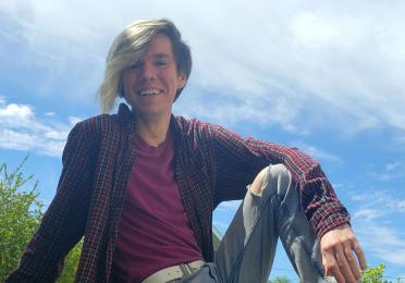 Drew sitting on a fence with his arm resting on his knee