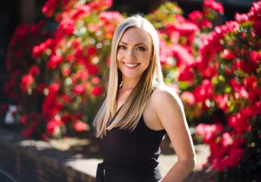 Courtney Porter smiles in front of red flowers 