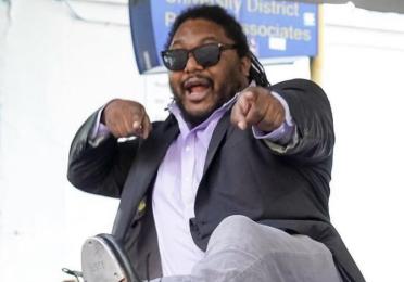 Alex Dugdale in tap shoes and sunglasses playfully pointing at the camera 