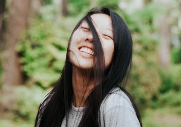 Anna lee shrugs and smiles with some hair blowing in her face 