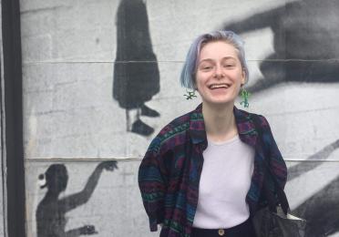 Kelly smiles in front of a wall 