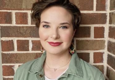 Brooke Thimmig in a green jacket infant of a brick wall 