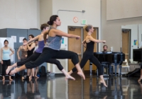 Dancers leaping in the studio, as musician plays piano