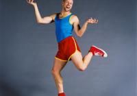 Bald man in bright athletic clothing humorously balances on one toe. 