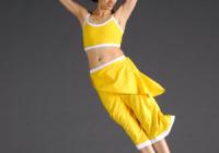 Lady in yellow jumps with arms in wide 'V' shape and legs straight and together. 