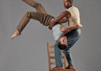 Jo stands on a chair while holding Fausto that is upside down. 
