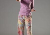 Julia stands face on in colorful pants. Her right arm is extended straight forward while her left arm is bent at the elbow near her hip. Her left knee is slightly bent and she looks to her right.