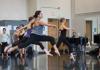 Dancers leaping in the studio, as musician plays piano