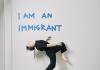 Alice dances front of a wall that says, "I am an immigrant" 