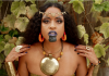 Brown skinned woman adorned in African gold jewelry and black paint. 