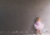 A little girl in ballet clothing standing at a wall 