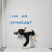 Alice dances front of a wall that says, "I am an immigrant" 