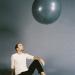A man sits casually on the floor staring the large sphere that is floating above. 