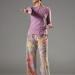 Julia stands face on in colorful pants. Her right arm is extended straight forward while her left arm is bent at the elbow near her hip. Her left knee is slightly bent and she looks to her right.